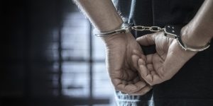 Arrested man in handcuffs with handcuffed hands behind back in prison